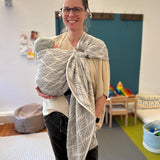 Woman holding a baby in a sling in a room with toys and furniture.