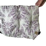 Fabric with purple moth pattern held by a hand on a beige background