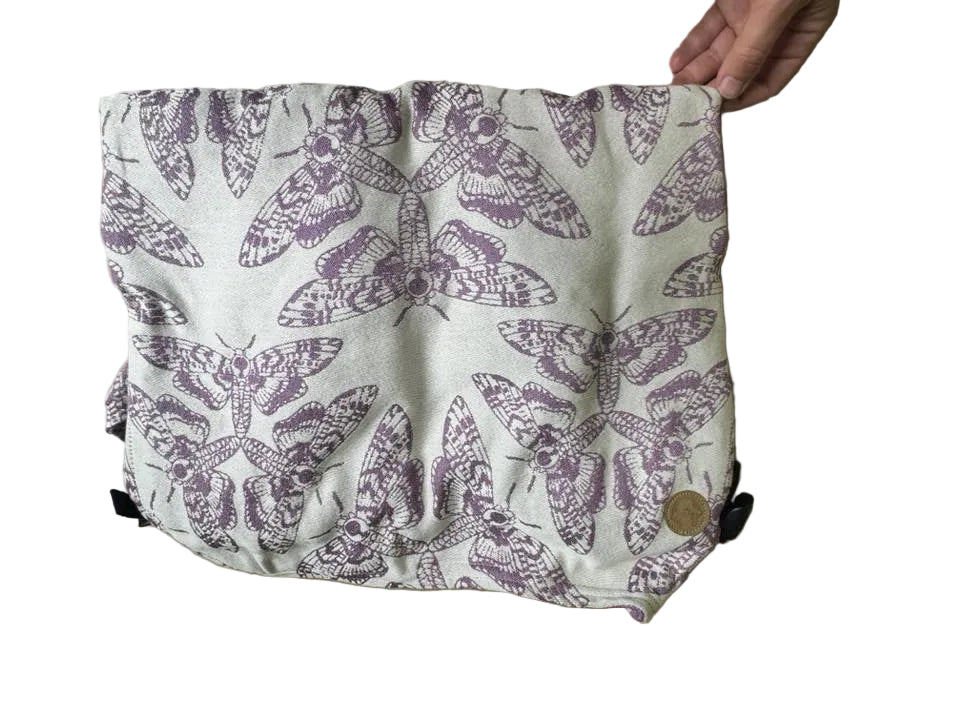 Fabric with purple moth pattern held by a hand on a beige background