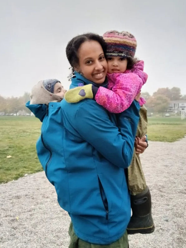 Woman in a blue coat holding two children outdoors on a cloudy day.