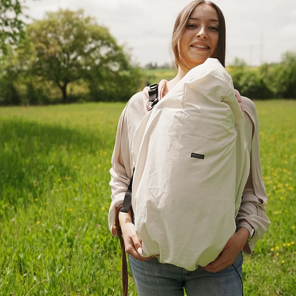Woman carrying a baby in a sling outdoors in a grassy field