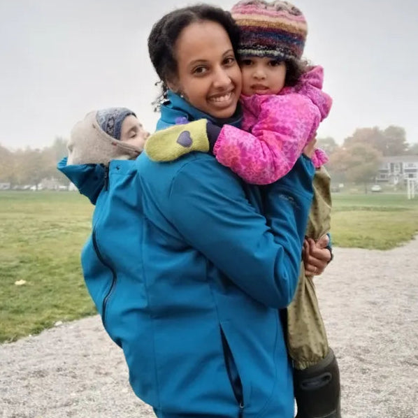 Woman in a blue coat holding two children outdoors on a cloudy day.