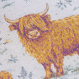 Close-up of a woven textile featuring Highland cows in golden yellow and brown tones on a light off-white background with muted blue-gray floral details.