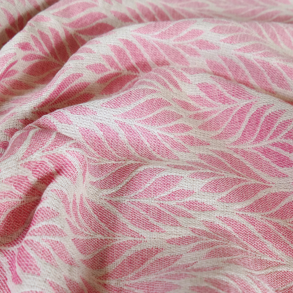 A close-up of a pink and off-white woven fabric with a repeating leaf or palm-like pattern, shown with soft folds and texture.